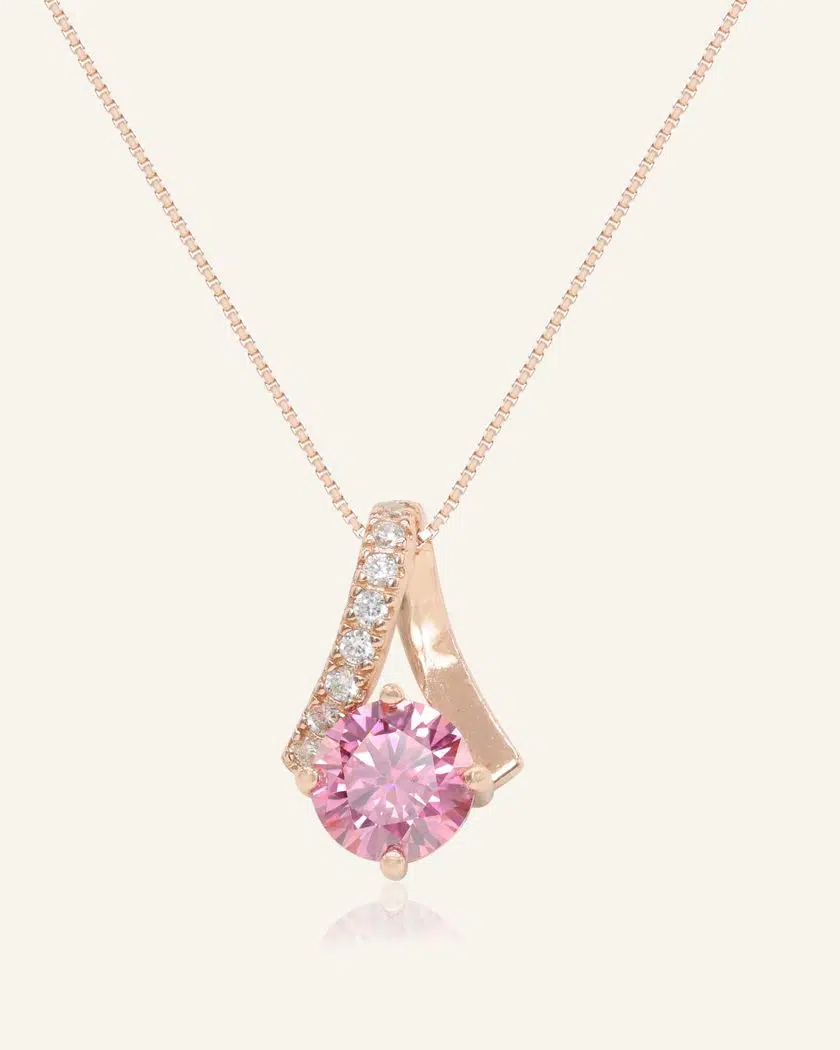 A rose gold necklace featuring a stunning 1-carat round pink moissanite centerpiece, accented with a graceful curved design adorned with sparkling cubic zirconias.