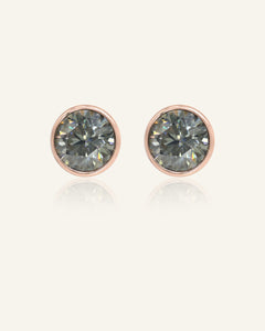 Close-up of the One Carat Gunmetal Grey Moissanite Bezel Stud Earrings in rose gold, resting on a warm linen background