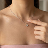 Close-up of a model pointing to the reversible clover necklace, featuring the luminous mother of pearl side.