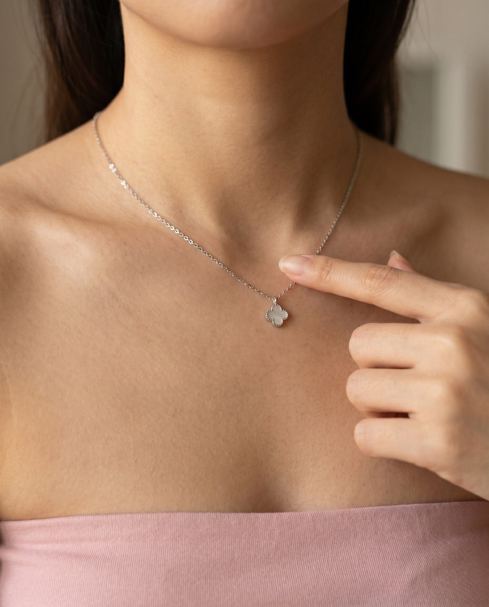 Close-up of a model pointing to the reversible clover necklace, featuring the luminous mother of pearl side.