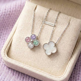 Two clover necklaces displayed in a boutique box, illustrating both the mother of pearl and multi-color moissanite reversible sides.
