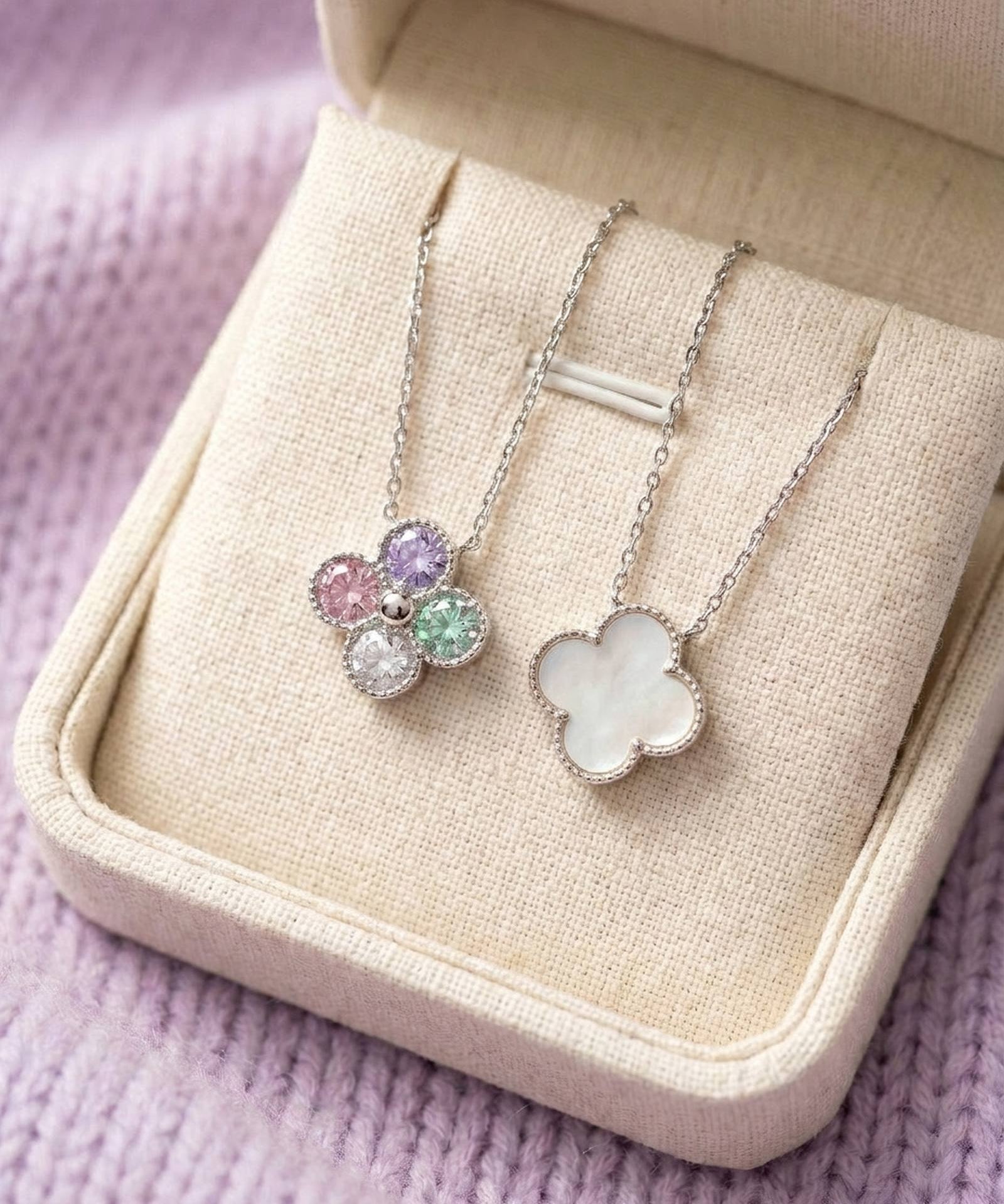 Two clover necklaces displayed in a boutique box, illustrating both the mother of pearl and multi-color moissanite reversible sides.