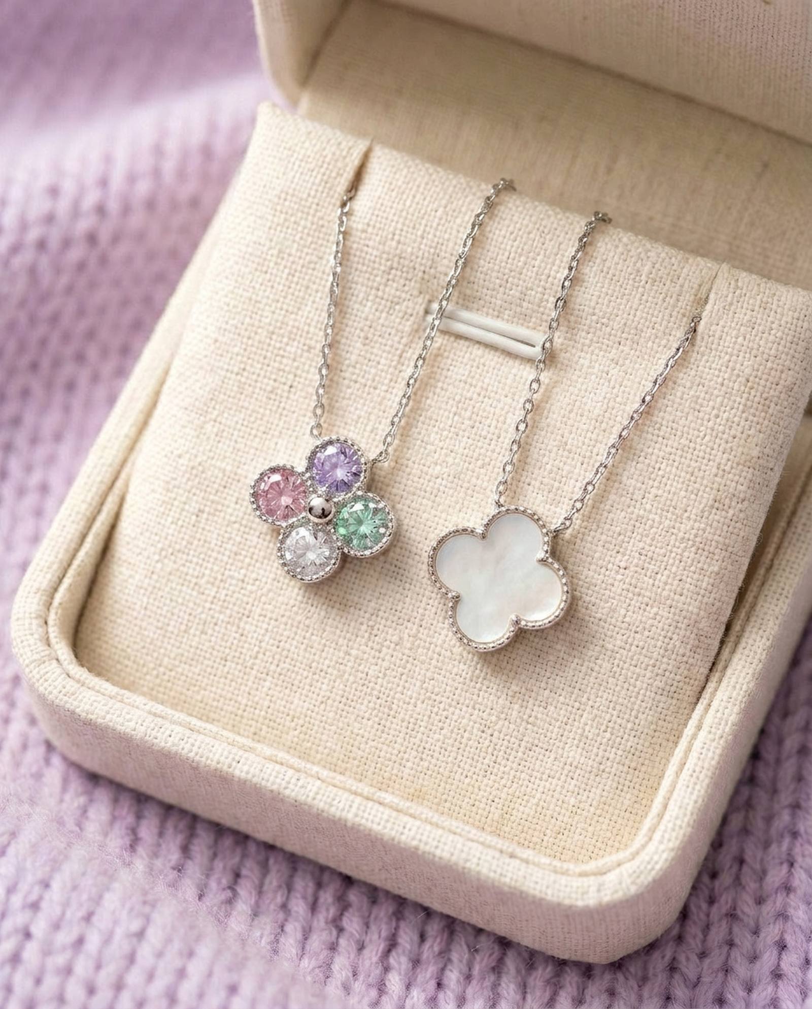 Two clover necklaces displayed in a boutique box, illustrating both the mother of pearl and multi-color moissanite reversible sides.