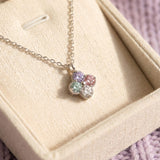 The A Tale of Two Clovers necklace resting in a premium cream jewelry box against a soft lavender knit background.