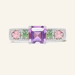 A silver ring featuring a central square-cut amethyst stone, flanked by two pink tourmalines and two green moissanites on either side, set in a textured band,