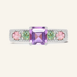 A silver ring featuring a central square-cut amethyst stone, flanked by two pink tourmalines and two green moissanites on either side, set in a textured band,