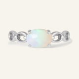 Astra Opal Ring in silver, resting on a warm linen background