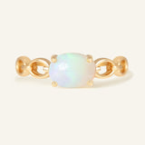 Astra Opal Ring in yellow gold, resting on a warm linen background