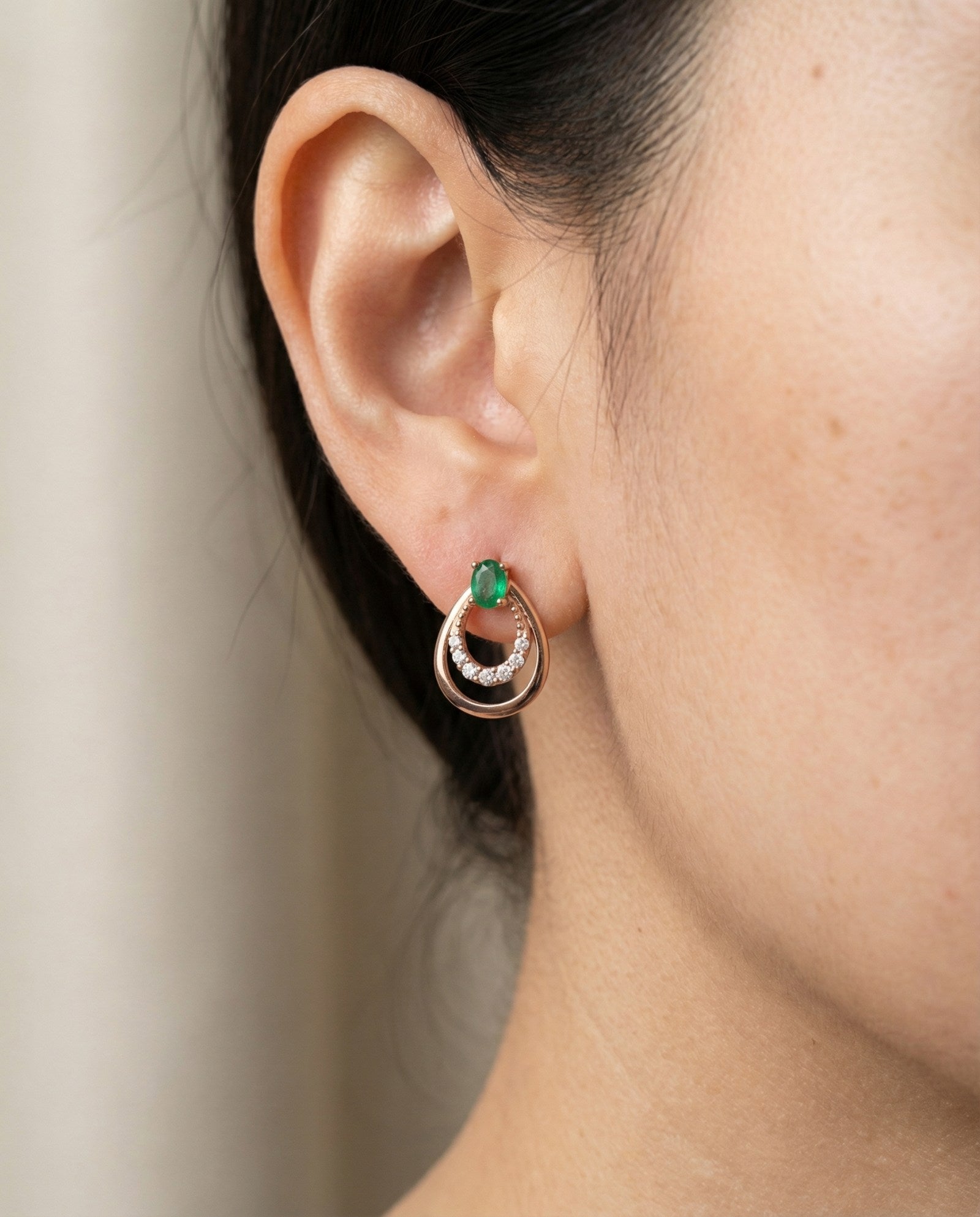 Lifestyle photo of a model wearing Aura Emerald Drop Studs in rose gold, highlighting the vibrant green natural emerald.