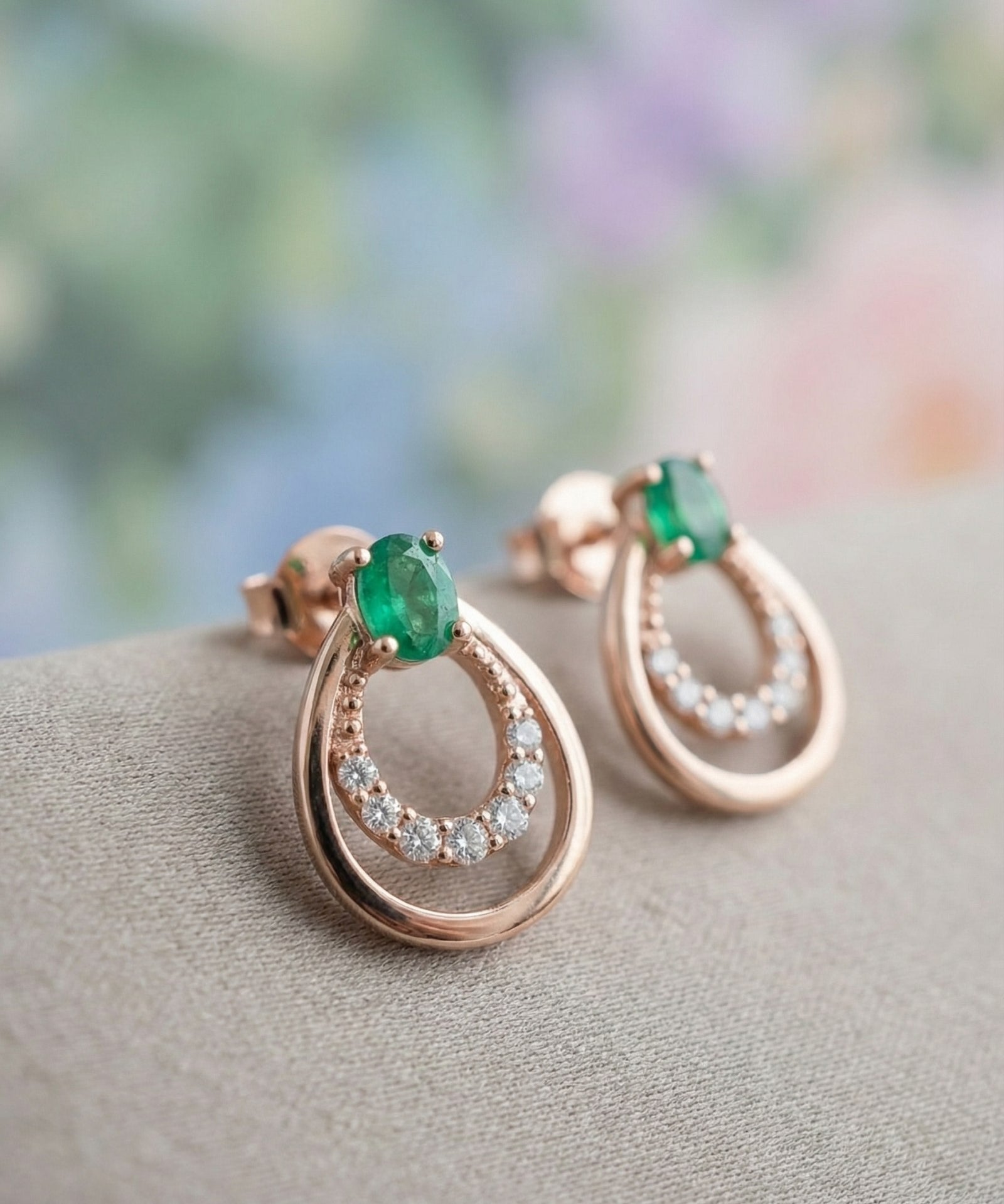 Macro view of the Aura Emerald Drop Studs in 18k Rose Gold showing the natural oval emerald and shimmering pavé halo.