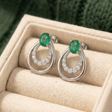 Pair of Aura Emerald Drop Studs in 925 Sterling Silver displayed in a luxury cream linen jewelry box.