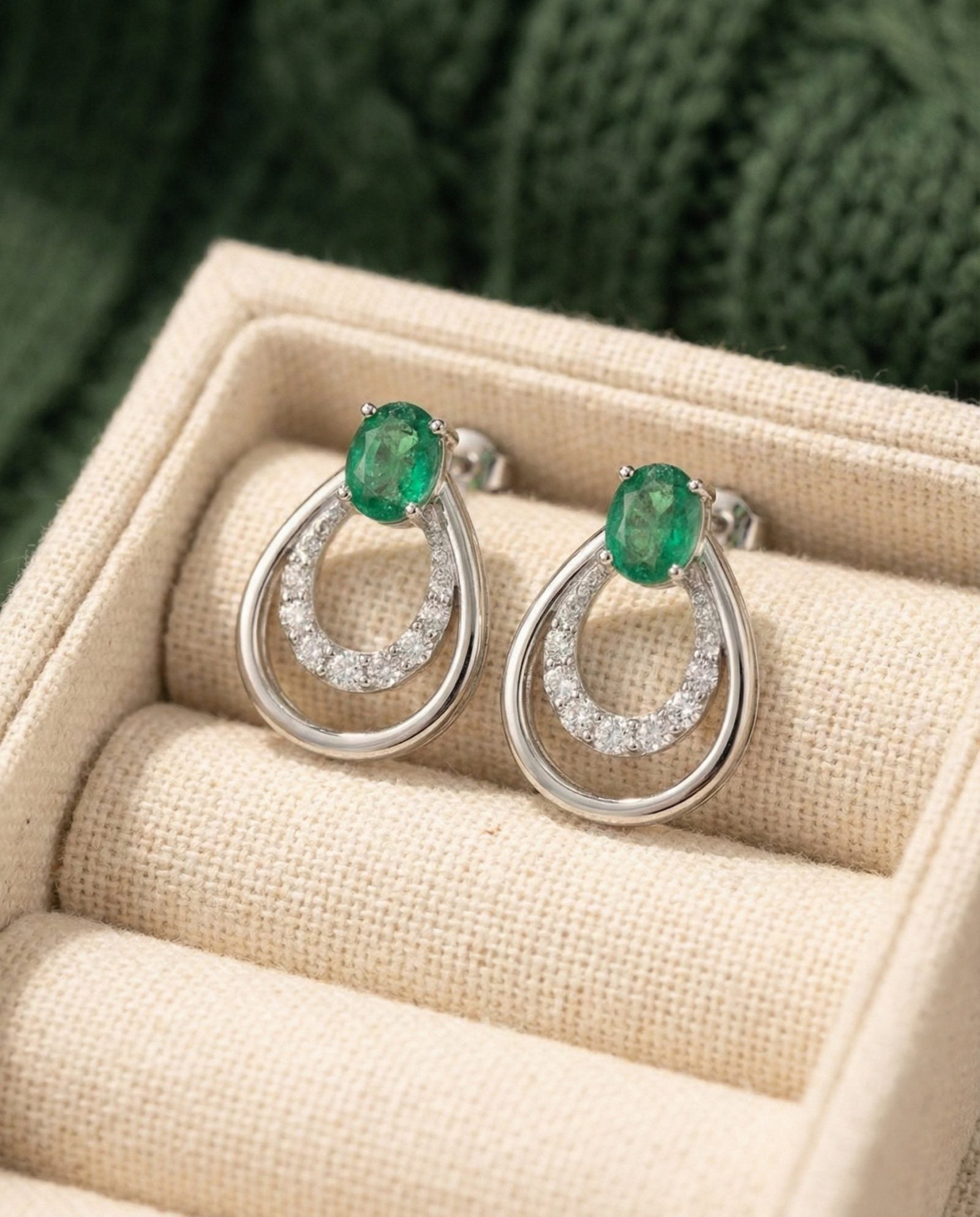 Pair of Aura Emerald Drop Studs in 925 Sterling Silver displayed in a luxury cream linen jewelry box.