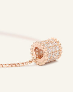 Barrel Necklace in rose gold, resting on a warm linen background
