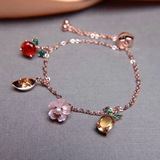 Rose gold slider bracelet featuring whimsical charms including a pineapple, orange, flower with pearl, and golden ingot, symbolizing blessings, wealth and joy.