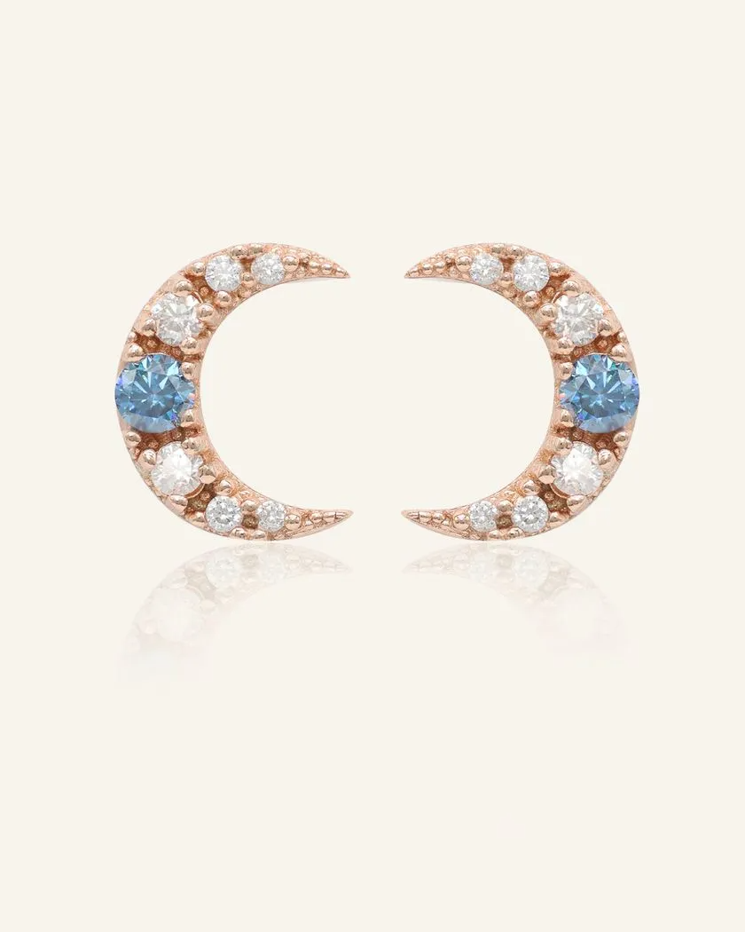 Celestial crescent moon studs in rose gold, featuring a dazzling blue moissanite accent surrounded by sparkling cubic zirconia for a radiant night-sky glow.