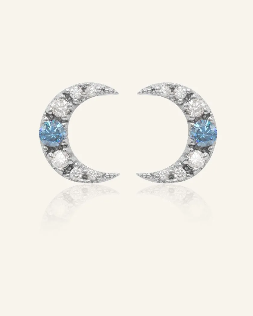 Celestial crescent moon studs in silver, featuring a dazzling blue moissanite accent surrounded by sparkling cubic zirconia for a radiant night-sky glow.