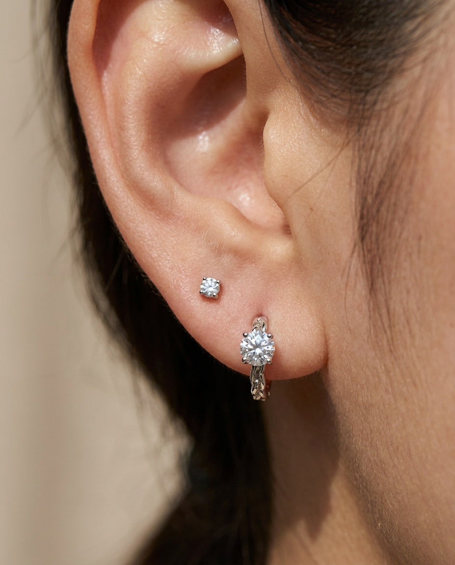 Close-up of a model wearing a silver Braided White Moissanite Huggie Hoop stacked with a small solitaire stud earring.