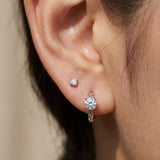 Close-up of a model wearing a silver Braided White Moissanite Huggie Hoop stacked with a small solitaire stud earring.