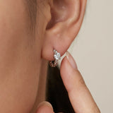 Close-up view of a hand touching a silver Braided White Moissanite Huggie Hoop worn in the ear lobe.