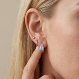 Model wearing a sterling silver Braided Sky Blue Moissanite Huggie Hoop stacked with a polished silver huggie in the earlobe.