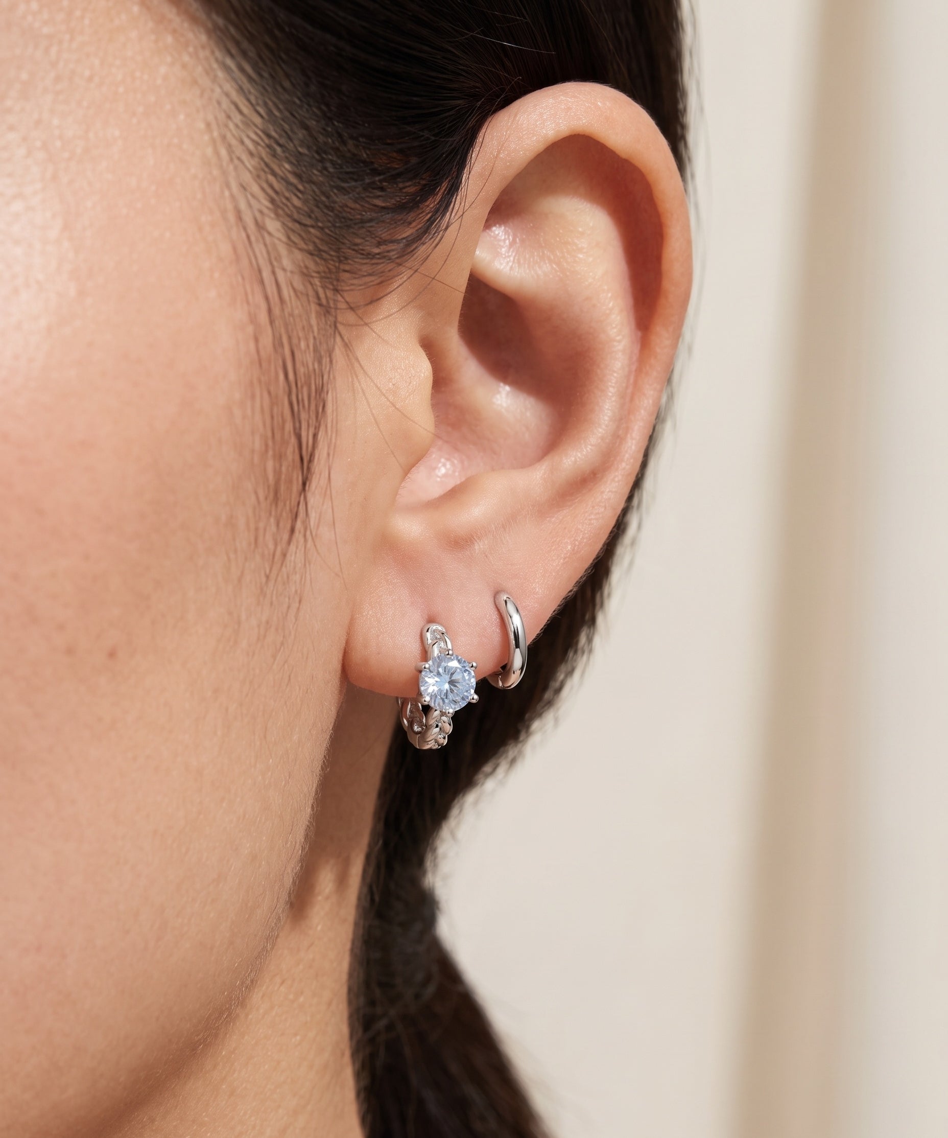 Close-up of a blonde model wearing a rose gold vermeil Braided Sky Blue Moissanite Huggie Hoop stacked with a small gold hoop and stud.