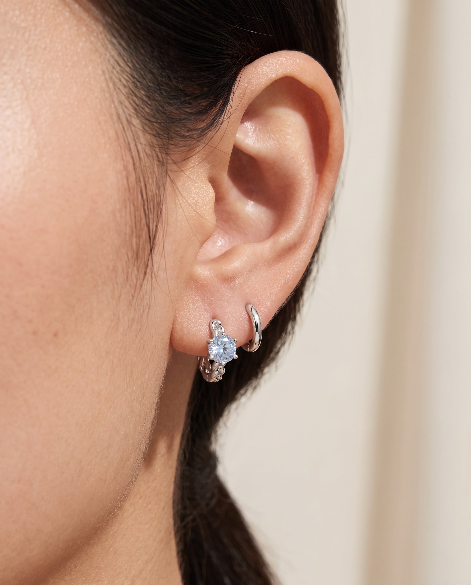 Close-up of a blonde model wearing a rose gold vermeil Braided Sky Blue Moissanite Huggie Hoop stacked with a small gold hoop and stud.