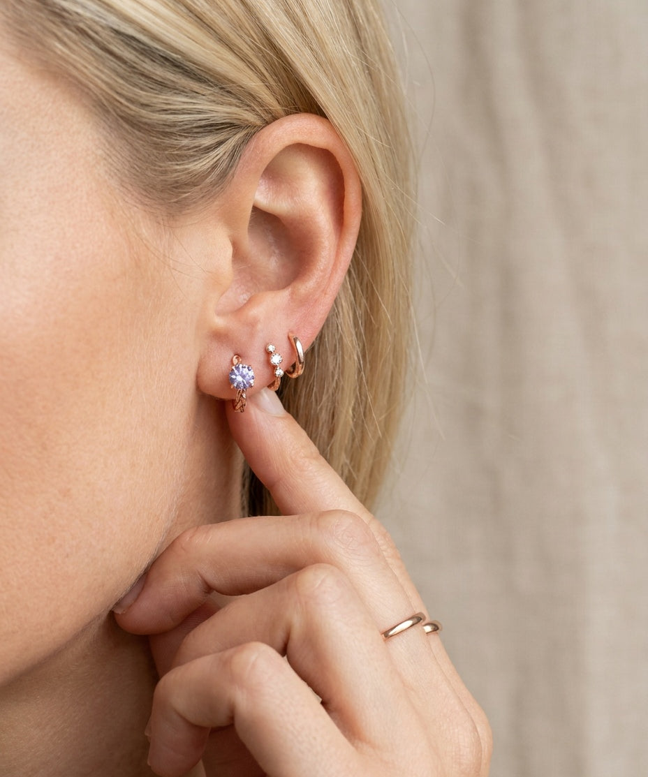 Profile view of a model wearing a rose gold vermeil Braided Lavender Moissanite Huggie Hoop in a curated ear stack.