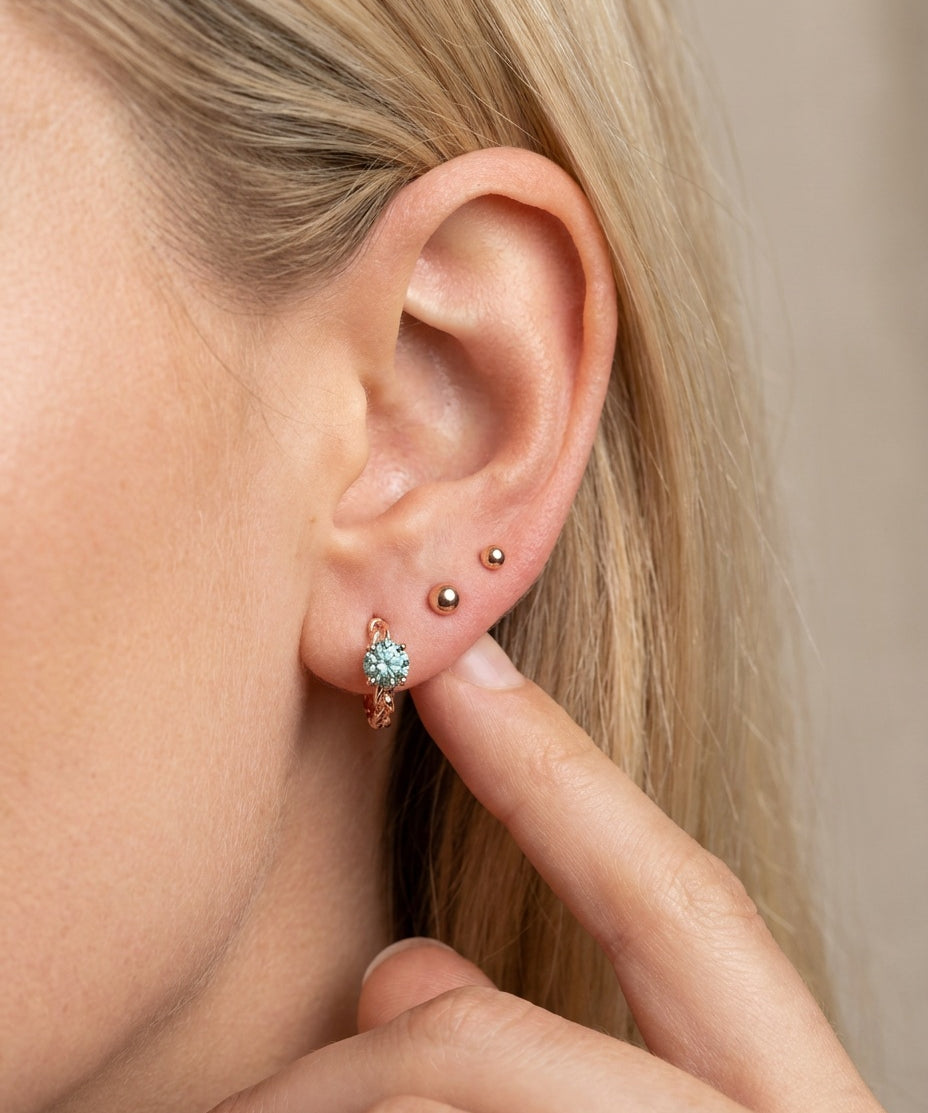Close-up of a blonde model wearing a rose gold vermeil Braided Mint Moissanite Huggie Hoop stacked with small gold ball studs.