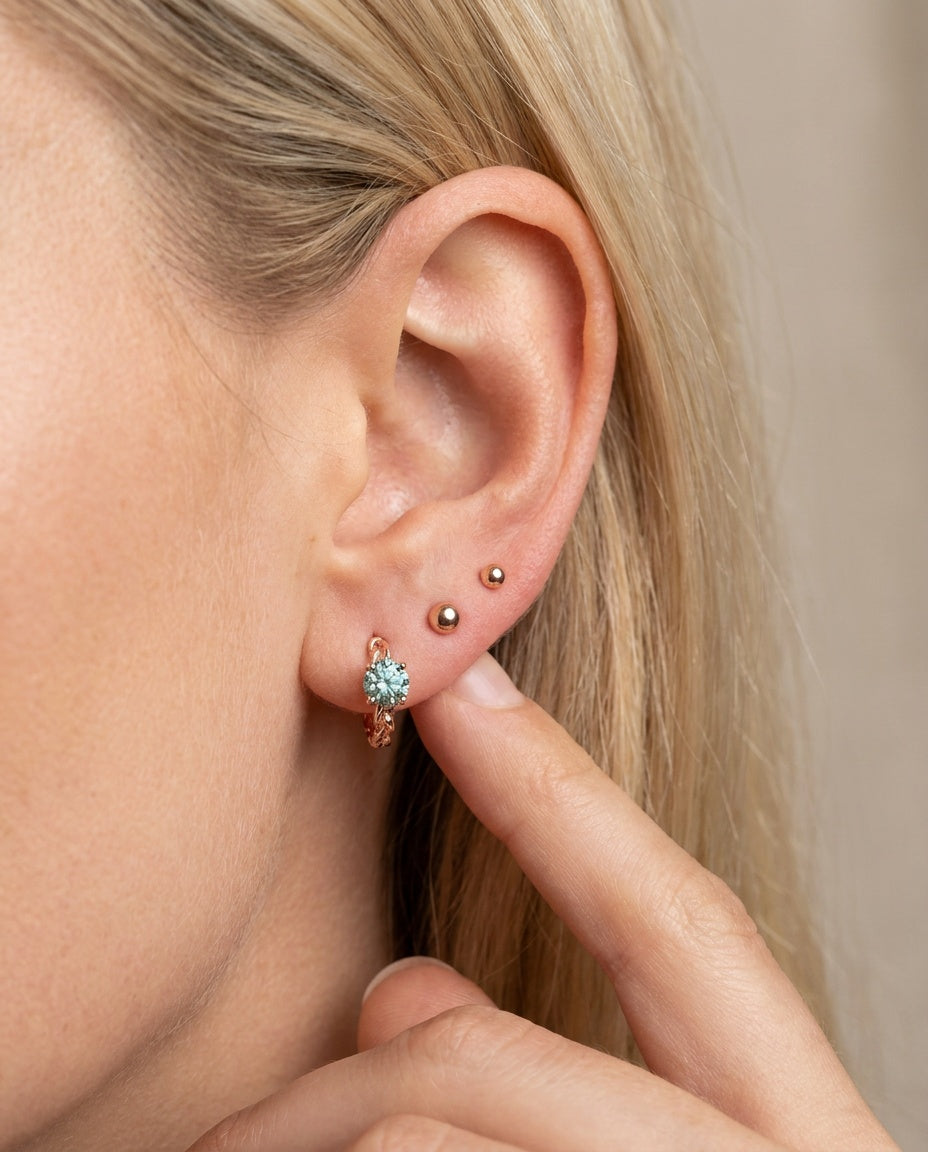 Close-up of a blonde model wearing a rose gold vermeil Braided Mint Moissanite Huggie Hoop stacked with small gold ball studs.