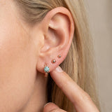 Close-up of a blonde model wearing a rose gold vermeil Braided Mint Moissanite Huggie Hoop stacked with small gold ball studs.
