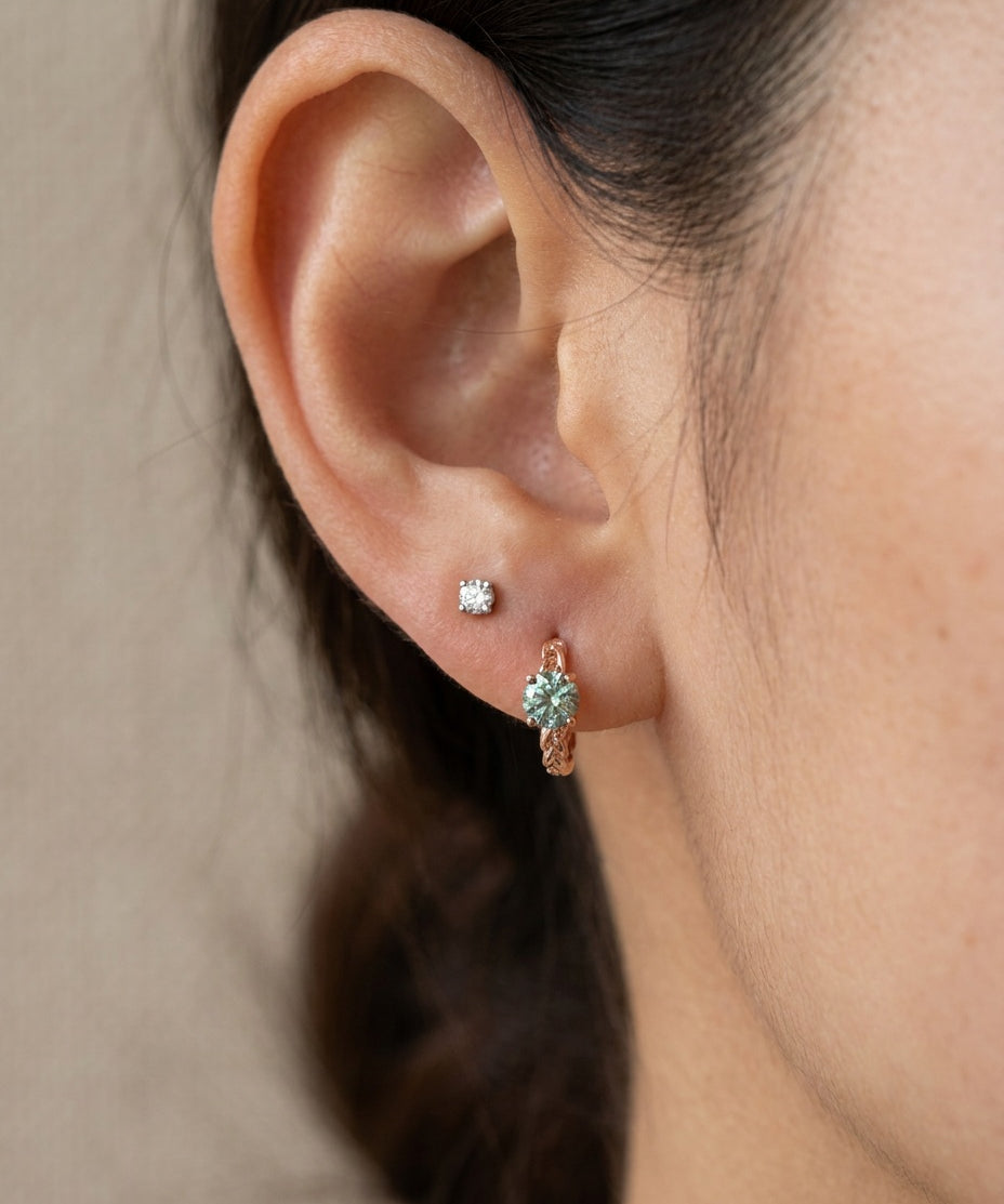 Model wearing a rose gold vermeil Braided Mint Moissanite Huggie Hoop paired with a single solitaire lobe stud.