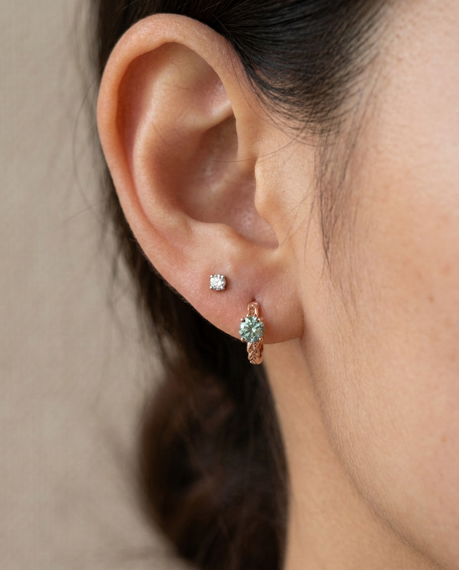Model wearing a rose gold vermeil Braided Mint Moissanite Huggie Hoop paired with a single solitaire lobe stud.