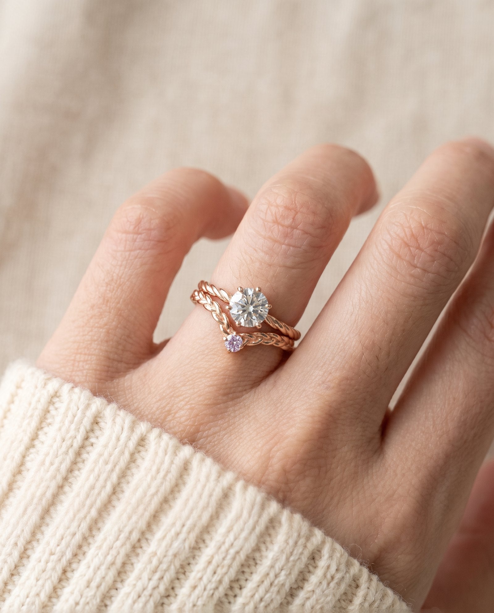 Model wearing a rose gold Braided Wishbone Lavender Moissanite Ring stacked below a large round solitaire engagement ring.