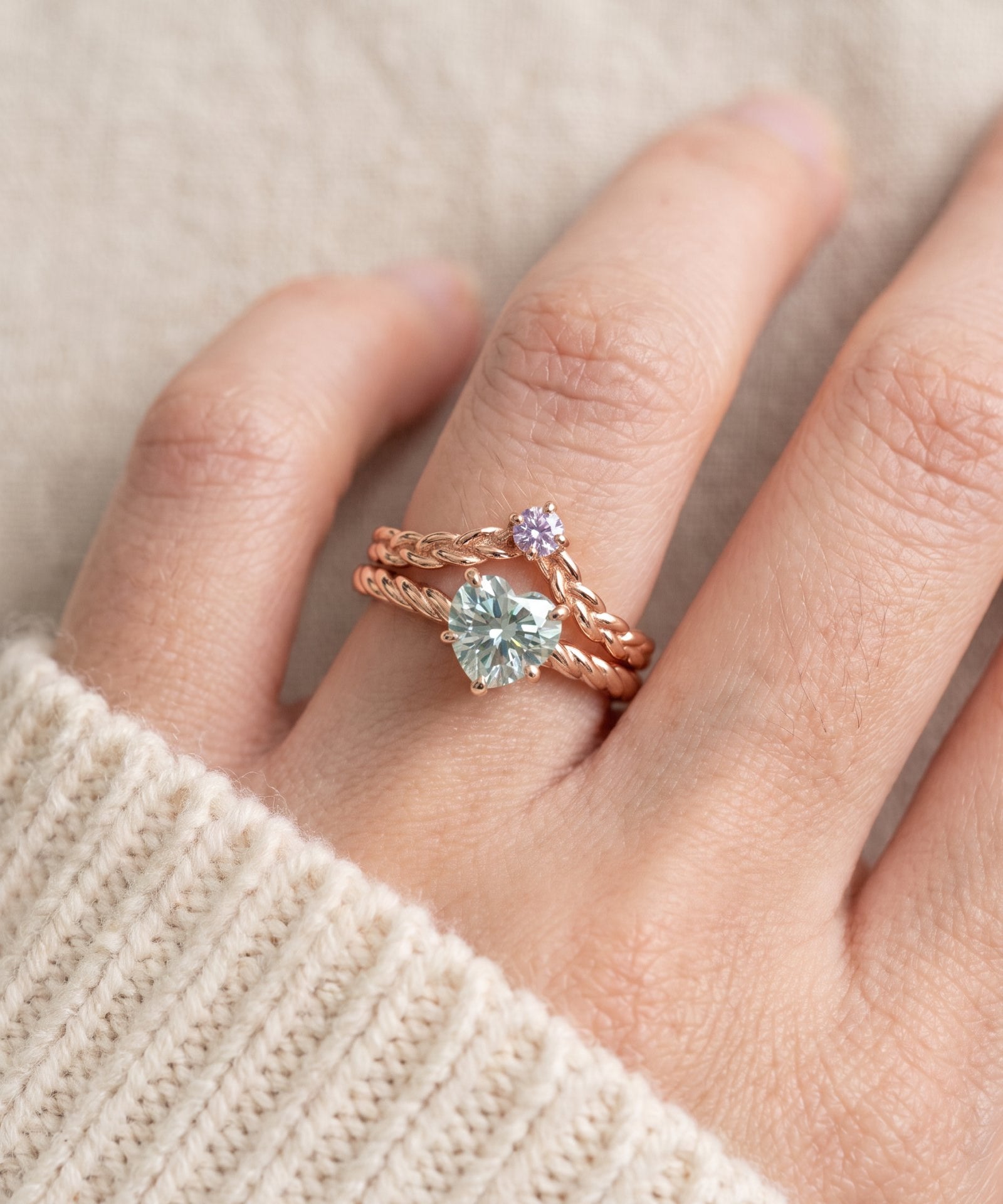 Model wearing a rose gold vermeil Braided Wishbone Lavender Moissanite Ring stacked above a large heart-cut moissanite solitaire ring.
