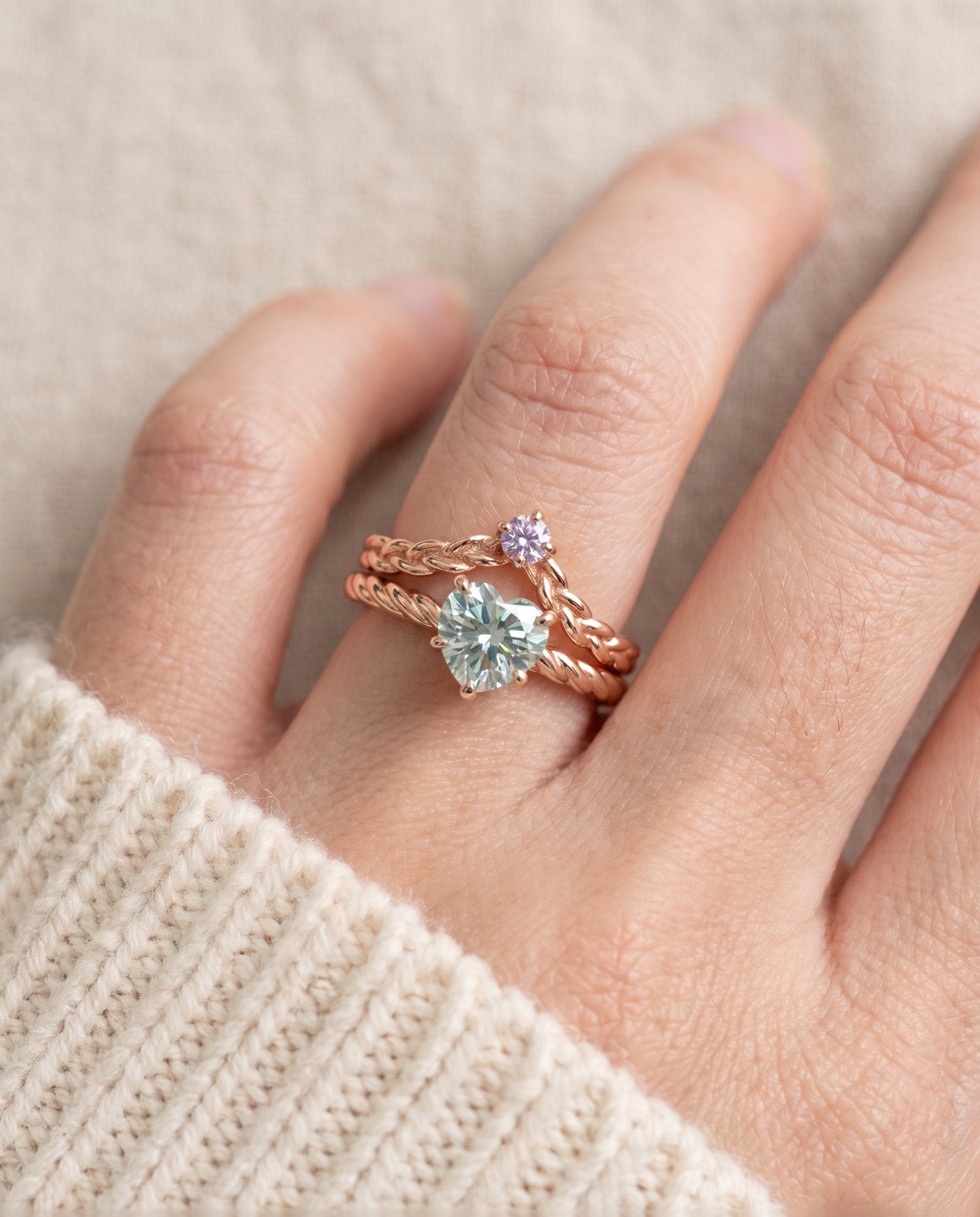 Model wearing a rose gold vermeil Braided Wishbone Lavender Moissanite Ring stacked above a large heart-cut moissanite solitaire ring.