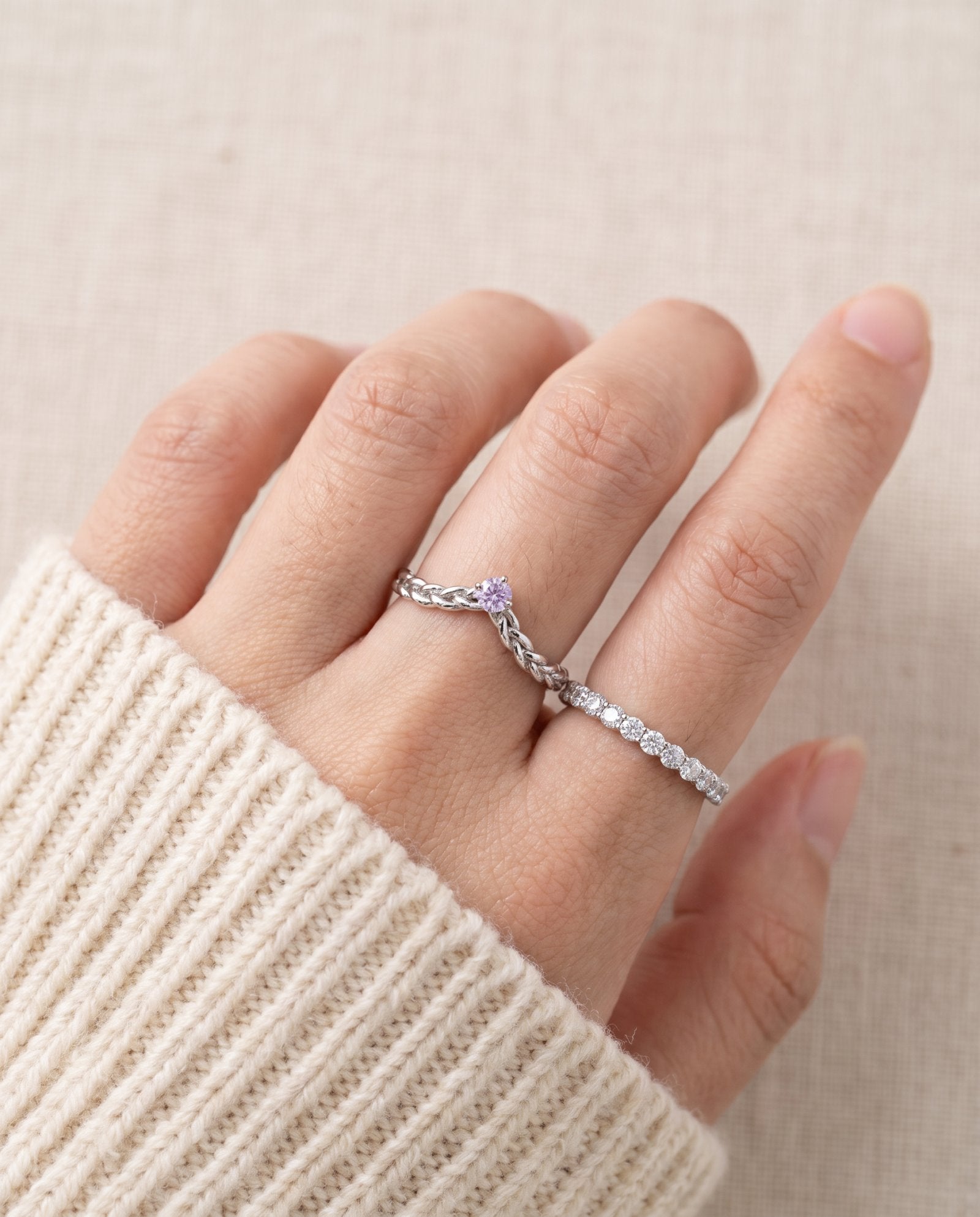 Model wearing a sterling silver Braided Wishbone Lavender Moissanite Ring stacked alongside a thin pave band.