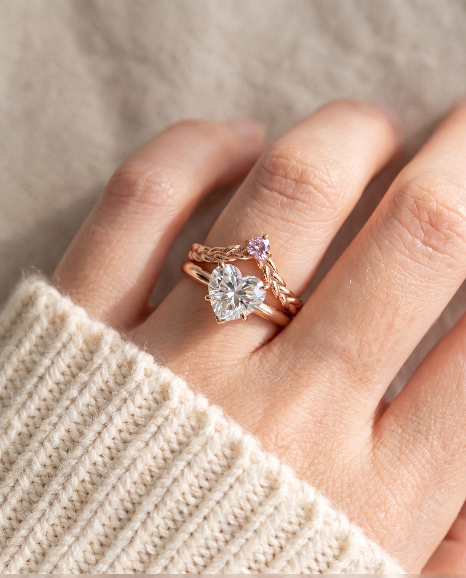 Model wearing a rose gold vermeil Braided Wishbone Pink Moissanite Ring stacked above a large heart-cut moissanite solitaire ring.