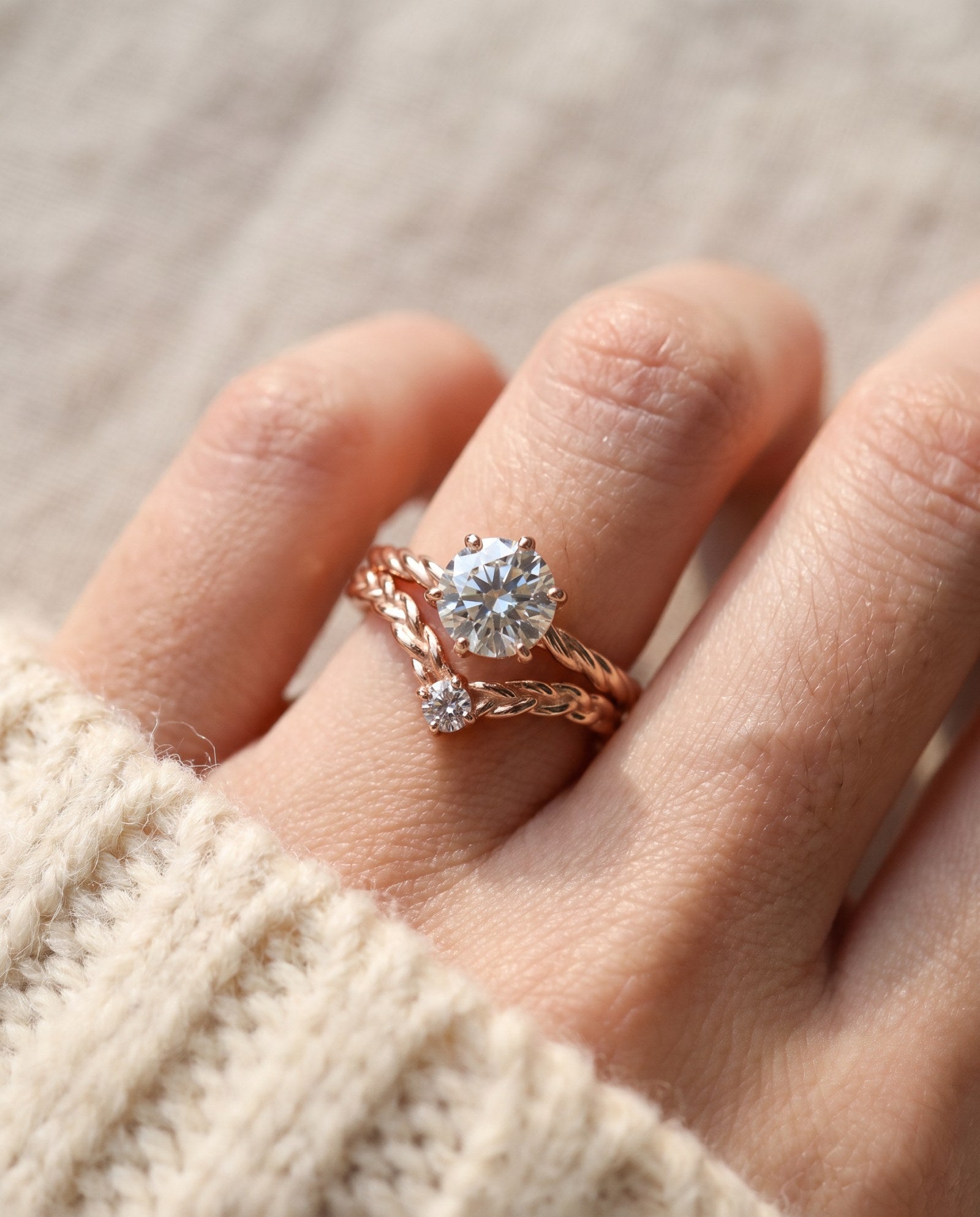 Model wearing a rose gold Braided Wishbone White Moissanite Ring stacked below a large round solitaire engagement ring.