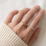 Model wearing a rose gold vermeil Braided Wishbone White Moissanite Ring on middle finger alongside a delicate eternity band.