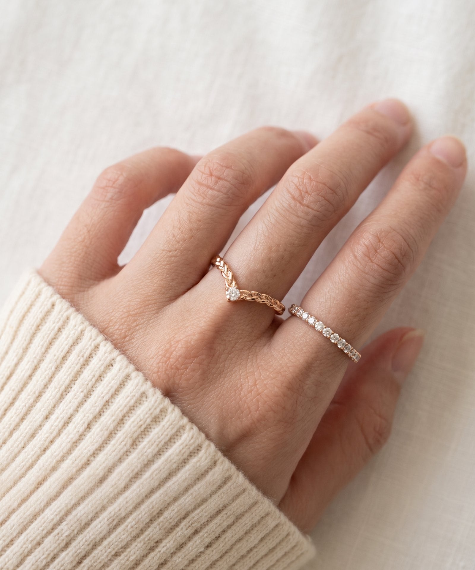 Model wearing a rose gold vermeil Braided Wishbone White Moissanite Ring on middle finger alongside a delicate eternity band.