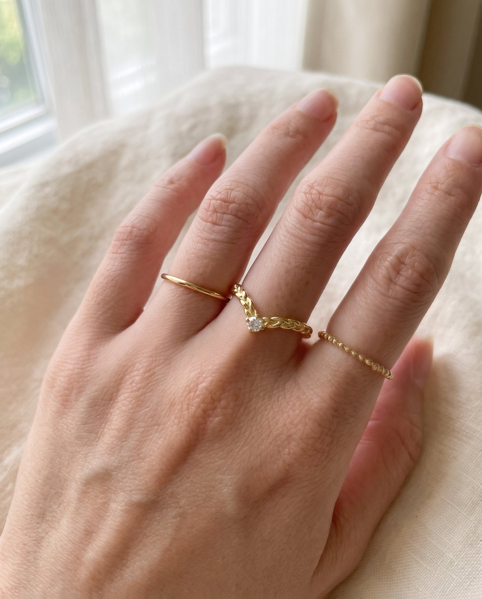 Model wearing a yellow gold vermeil Braided Wishbone White Moissanite Ring styled on middle finger between simple gold bands.