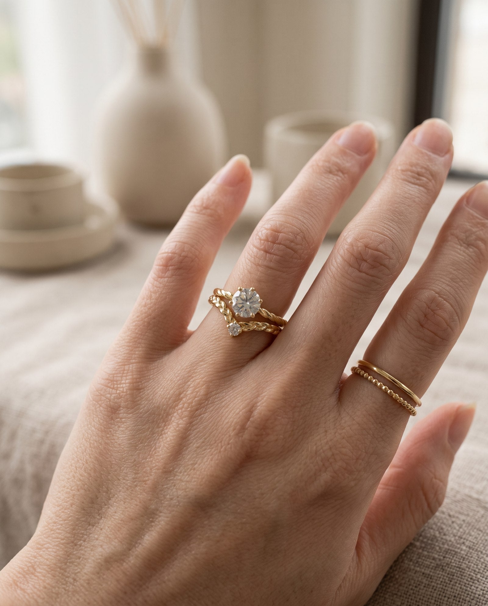 Model wearing a yellow gold Braided Wishbone White Moissanite Ring stacked below a round solitaire ring with simple gold bands.