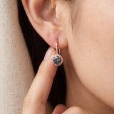 Macro shot of a hand gently touching a rose gold Twilight Grey moissanite halo drop earring.