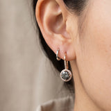 Close-up view of a model wearing a rose gold Twilight Grey moissanite halo ear hook stacked with a small silver huggie hoop.