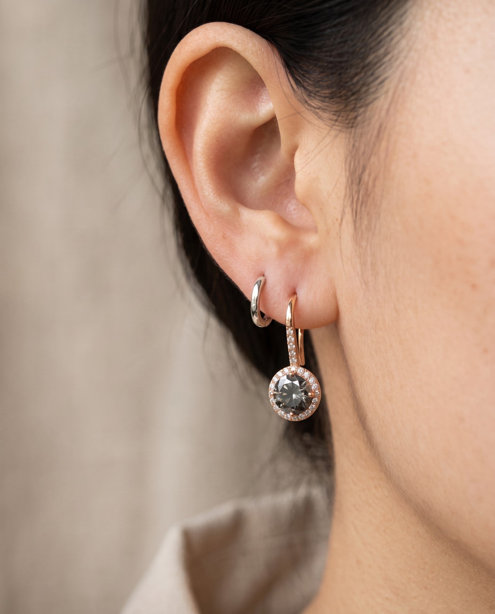Close-up view of a model wearing a rose gold Twilight Grey moissanite halo ear hook stacked with a small silver huggie hoop.