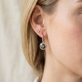 Side-profile view of a blonde model wearing yellow gold Candlelight Halo Moissanite Ear Hooks in Twilight Grey.