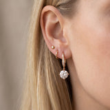 Lifestyle view of a model wearing a rose gold moissanite dangle ear hook stacked alongside small gold huggie hoops.