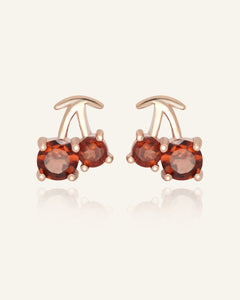 Cherry Garnet Studs in rose gold, resting on a warm linen background