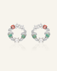 Close-up of the Mistletoe Wreath Studs in silver, resting on a warm linen background