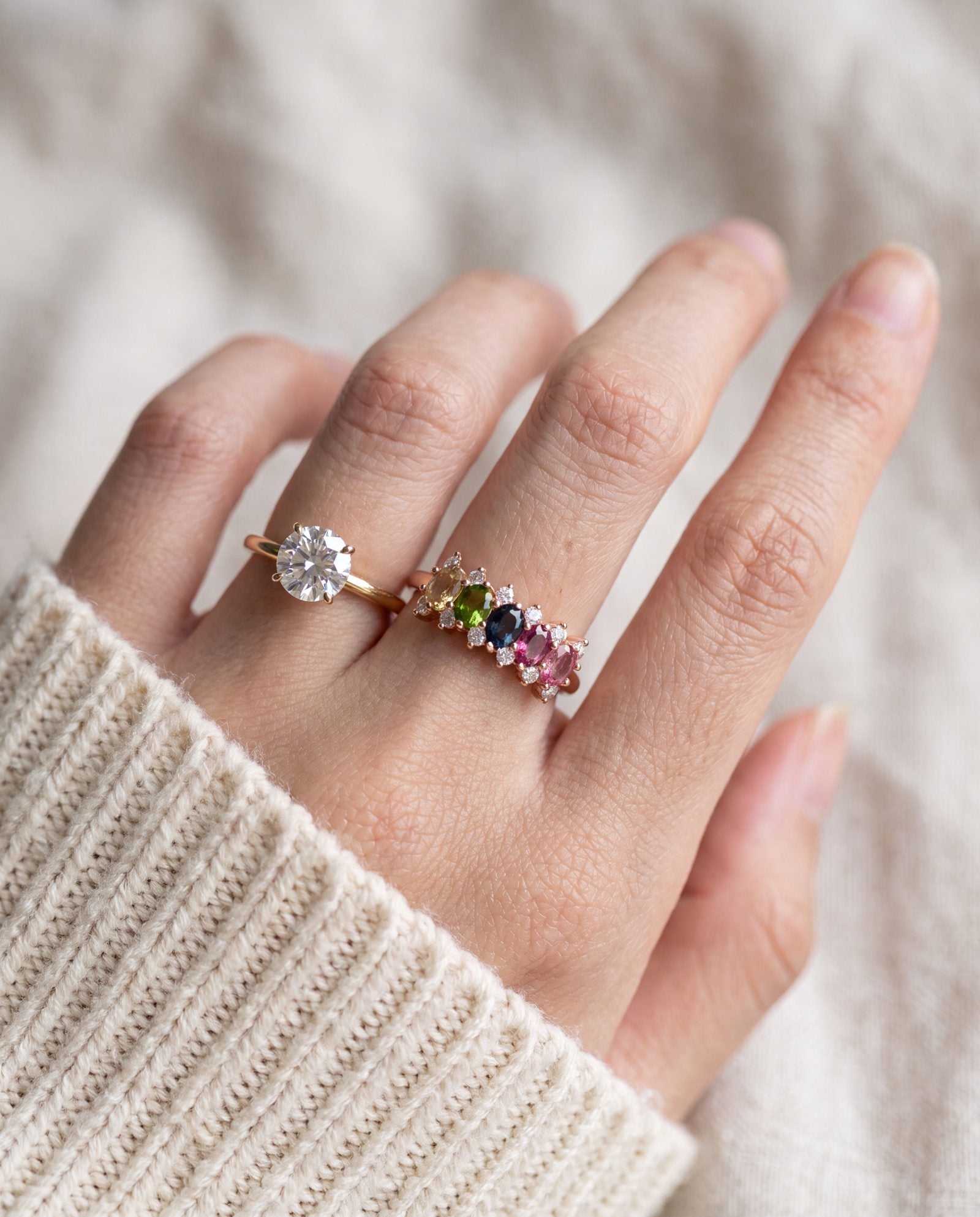 Model wearing a rose gold multi-colored oval stone ring stacked beside a solitaire moissanite ring.